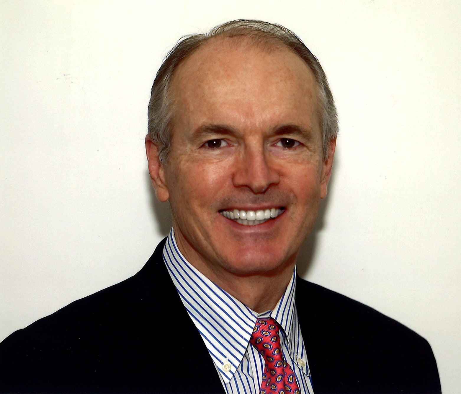 a man smiles in a black suit with white shirt and red tie