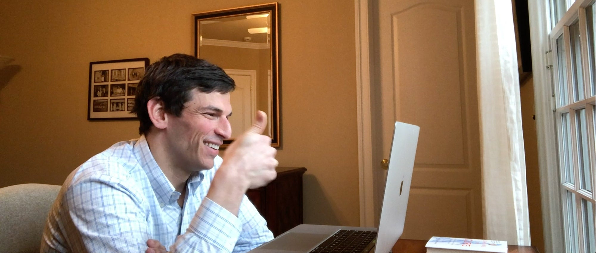 Dr. David Fajgenbaum seated at his laptop giving a thumbs up while participating in a video conference call
