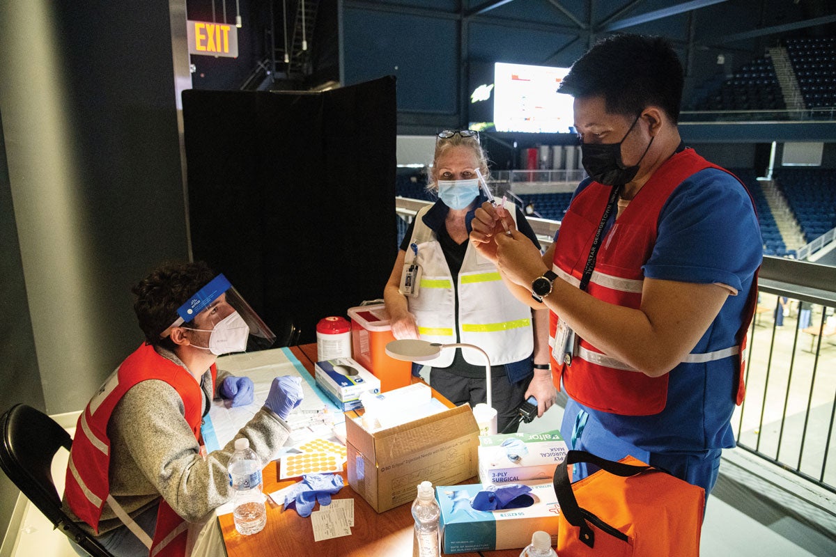 Dr. Ranit Mishori (center), medical director at the COVID-19 high-capacity vaccination site at D.C.’s Entertainment and Sports Arena, observes as Leon Padil- lia, nurse for MedStar Georgetown Student Health Center, instructs a medical student on how to prepare a dose of COVID-19 vaccine.
