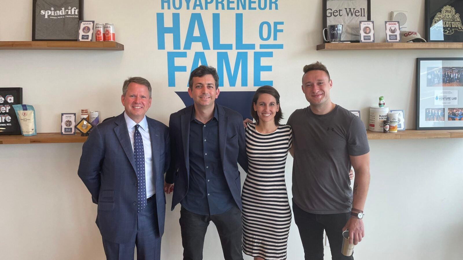 Michael Brown, Emily Owen, Etai Mizrav, and Mackenzie Copley stand in the Georgetown Vanture Lab in front of a wall reading “Hoyapreneur Hall of Fame.”