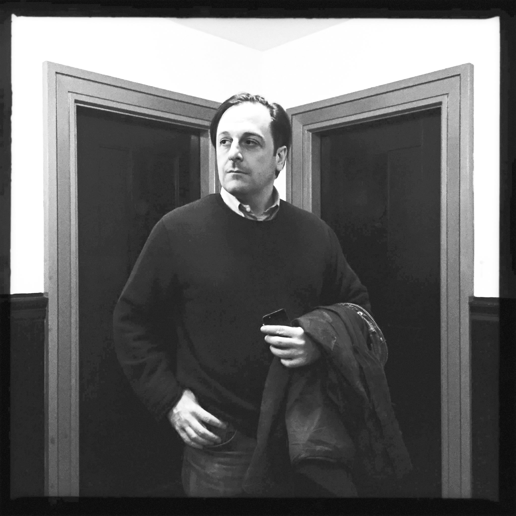 a black and white image of a man in a sweater between two doorways