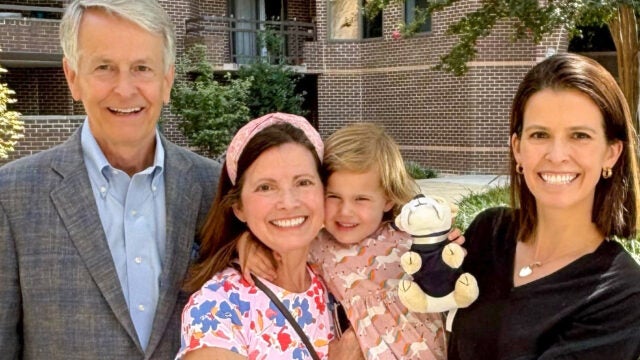 two women, a toddler and a man in a gray suit stand with each other